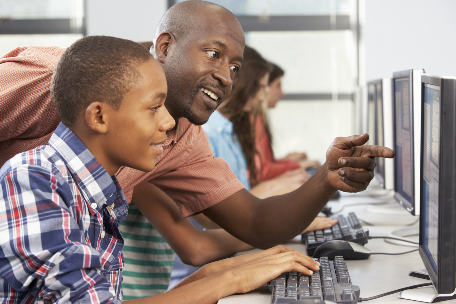 Teacher Helping Students Working at Computers in Classroom